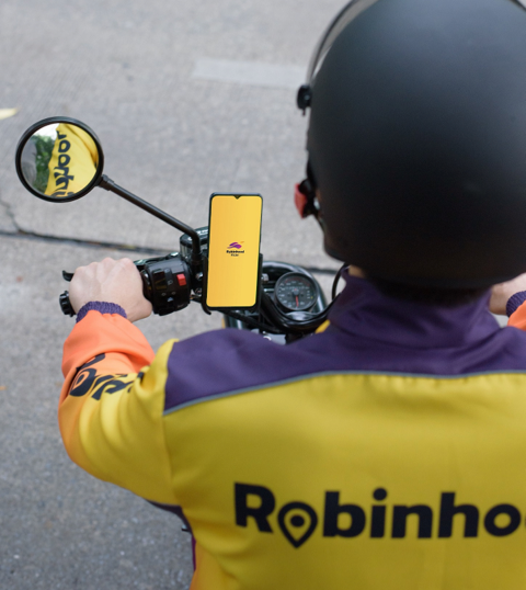 A Robinhood delivery driver looks at his smartphone which is fixed to the handlebars of his scooter.