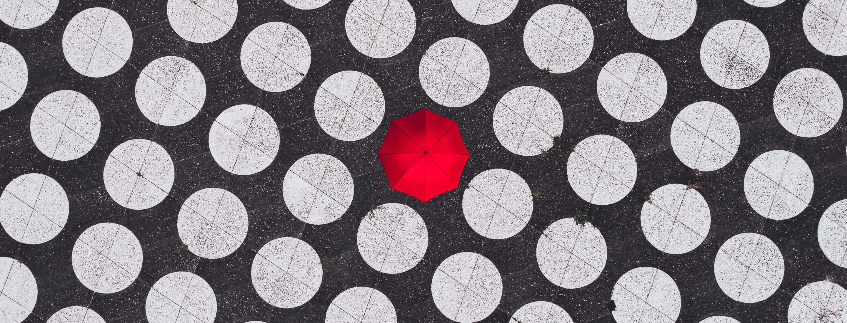 A single, red umbrella stands out from many empty, plain white tables