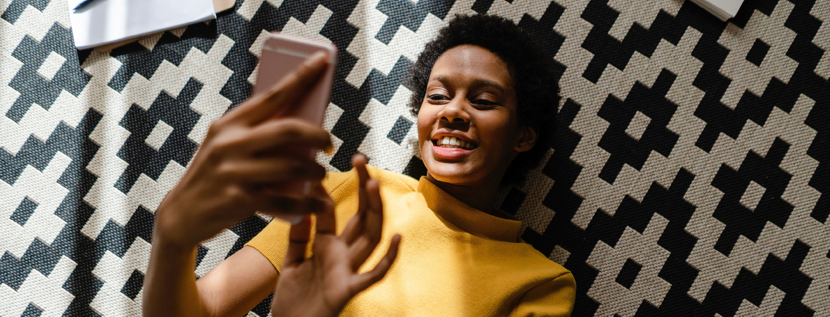 A women lays on her back, smiling while banking on her mobile phone