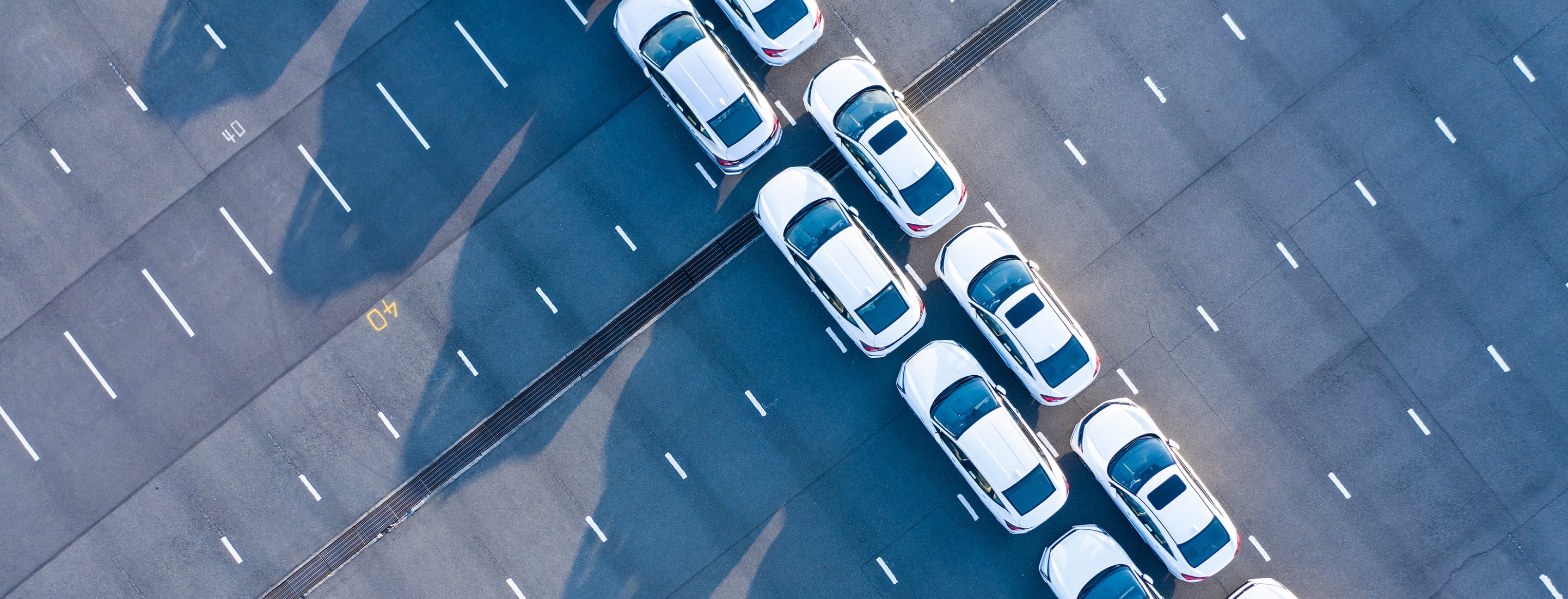 Aerial image of two rows of white vehicles lined up in a parking lot
