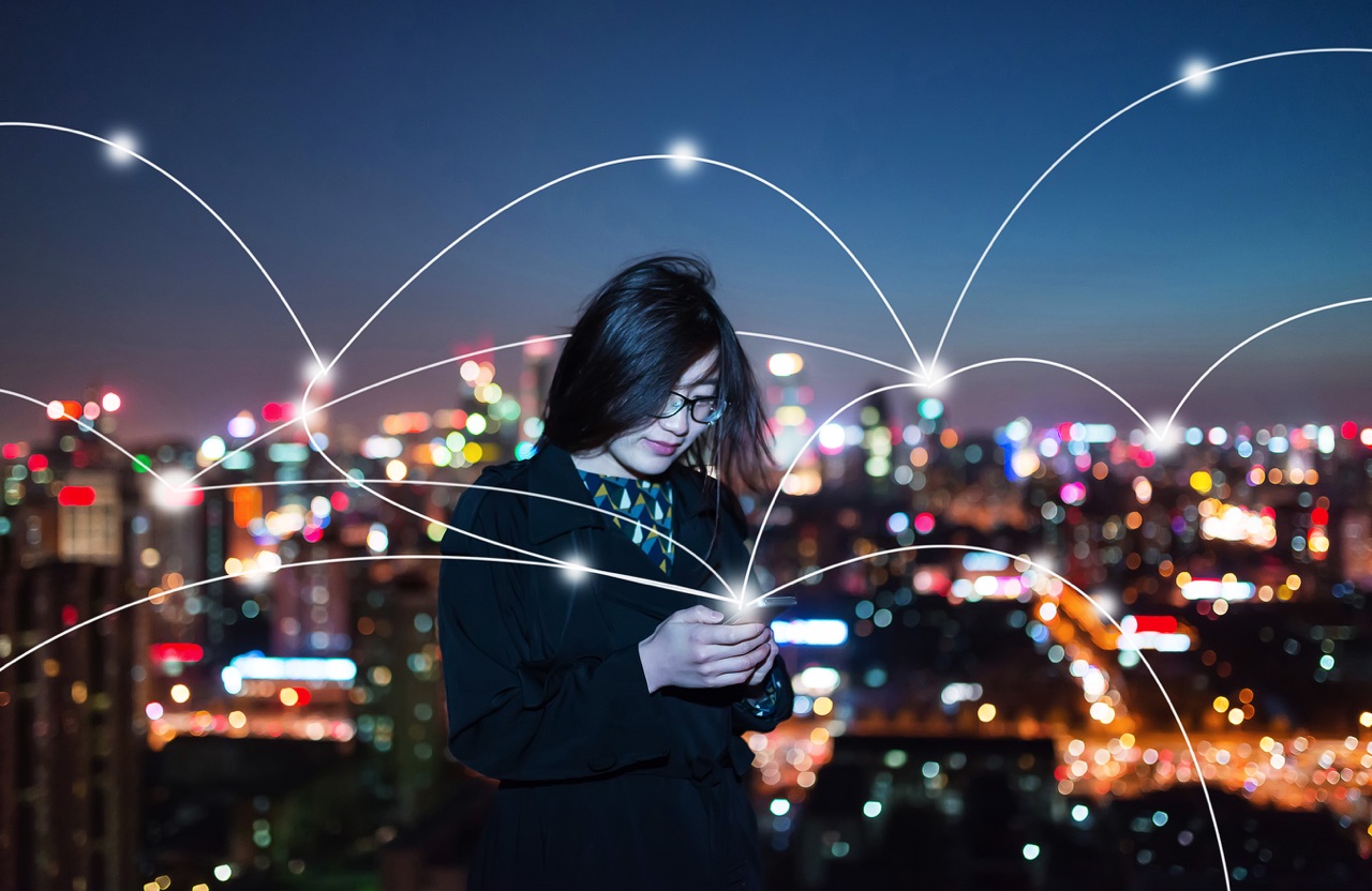 woman with mobile phone in front of a city that appears to be digitally connected