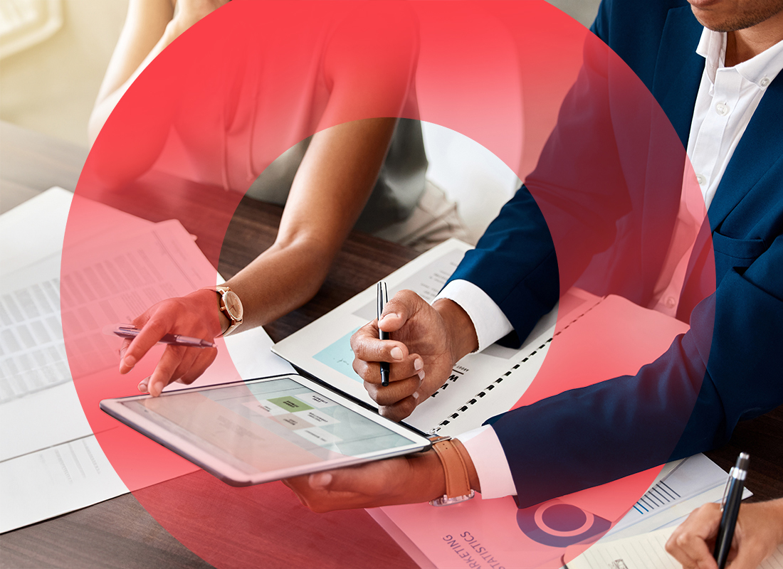Two business professionals seated at a desk, reviewing content on tablet.  The man is holding the tablet and a pen, while the woman is holding a pen and touching the tablet.