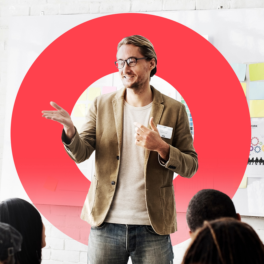 Middle aged man wearing glasses talking in front of a crowd of people