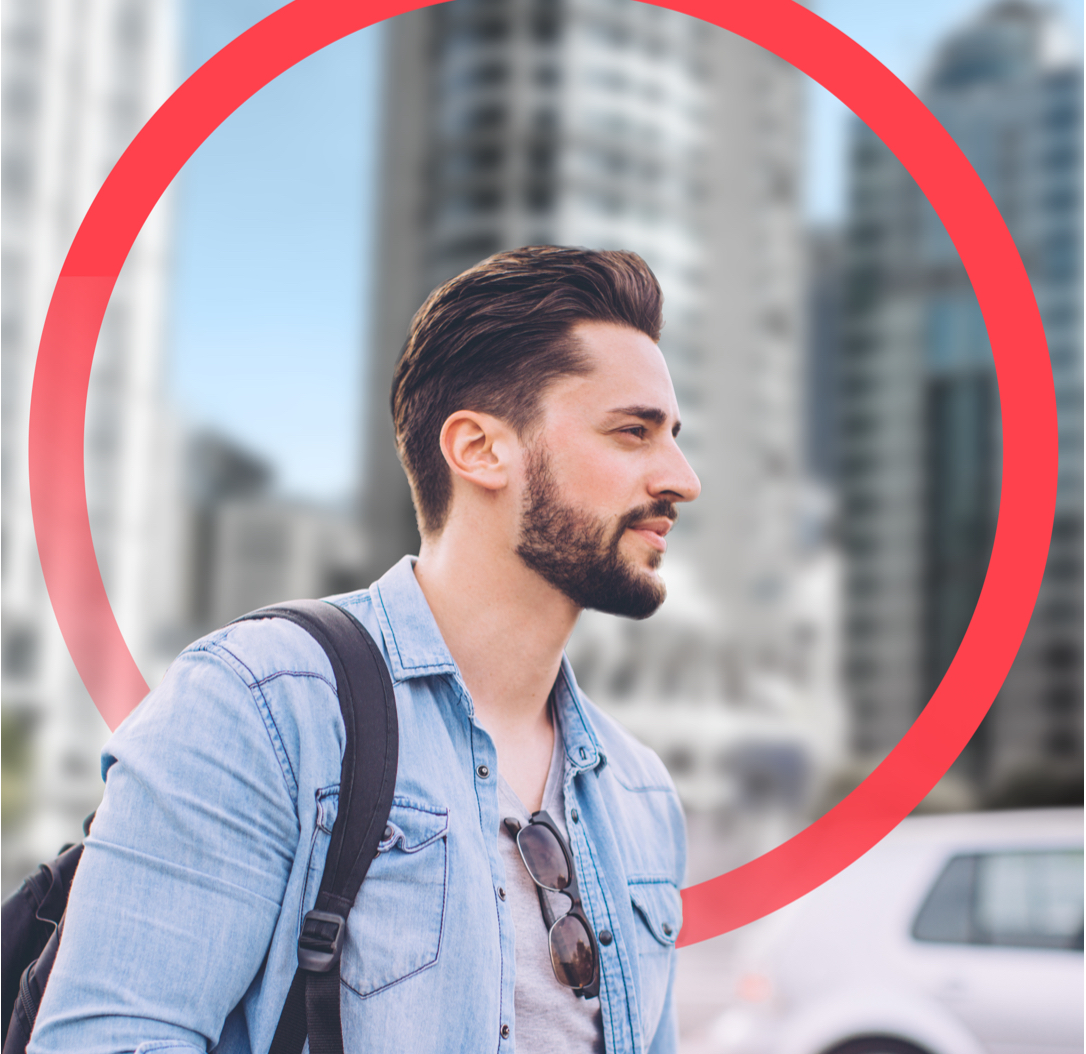 Young male professional walking on downtown business street with backpack and phone in hand; with a car in background