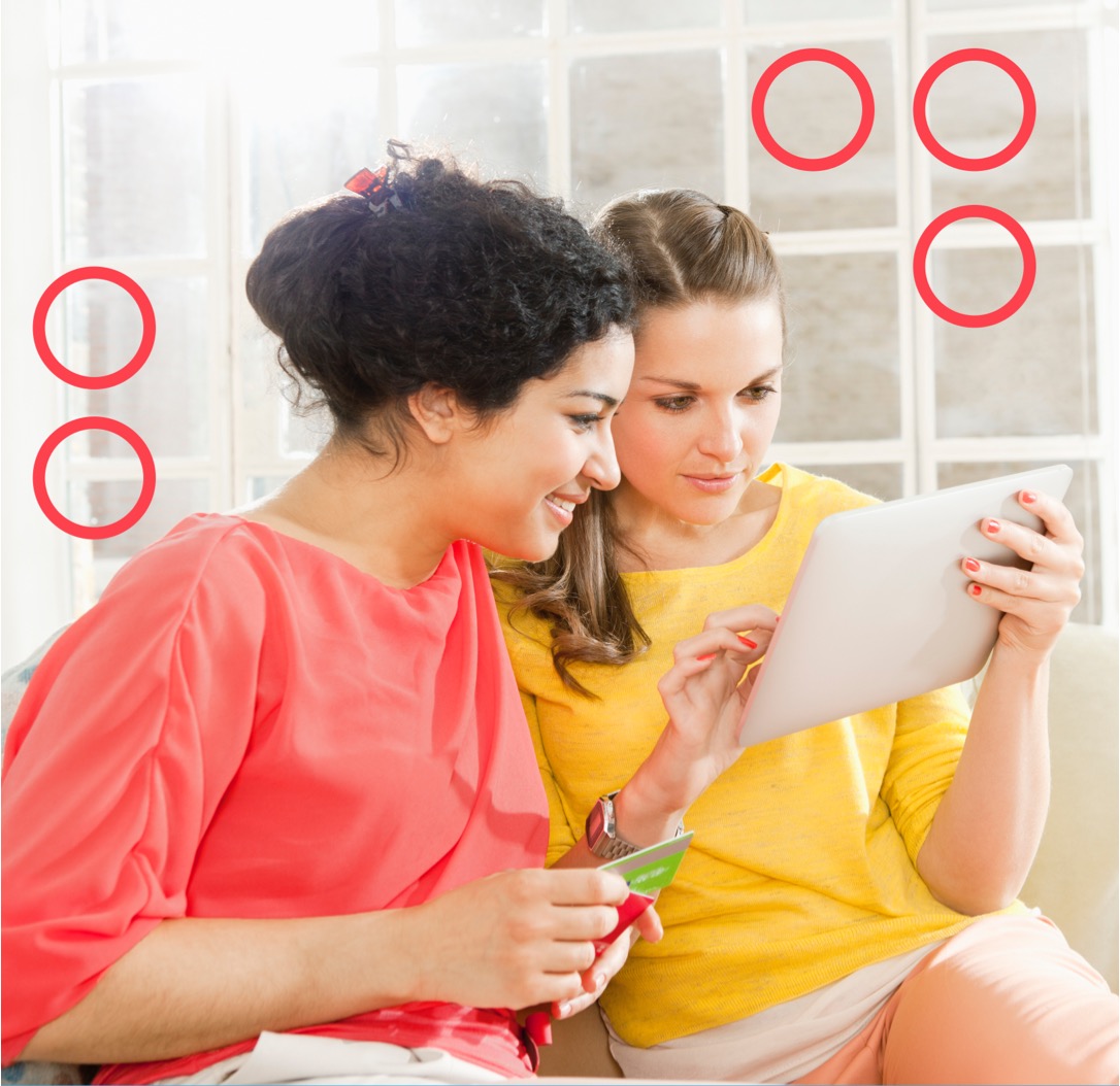 Two females sitting together, one holding a table while the other smiles and looks at the tablet