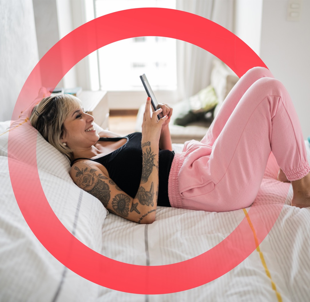 Casually dressed woman with tattoos on shoulder and arm, smiling while using mobile device on bed