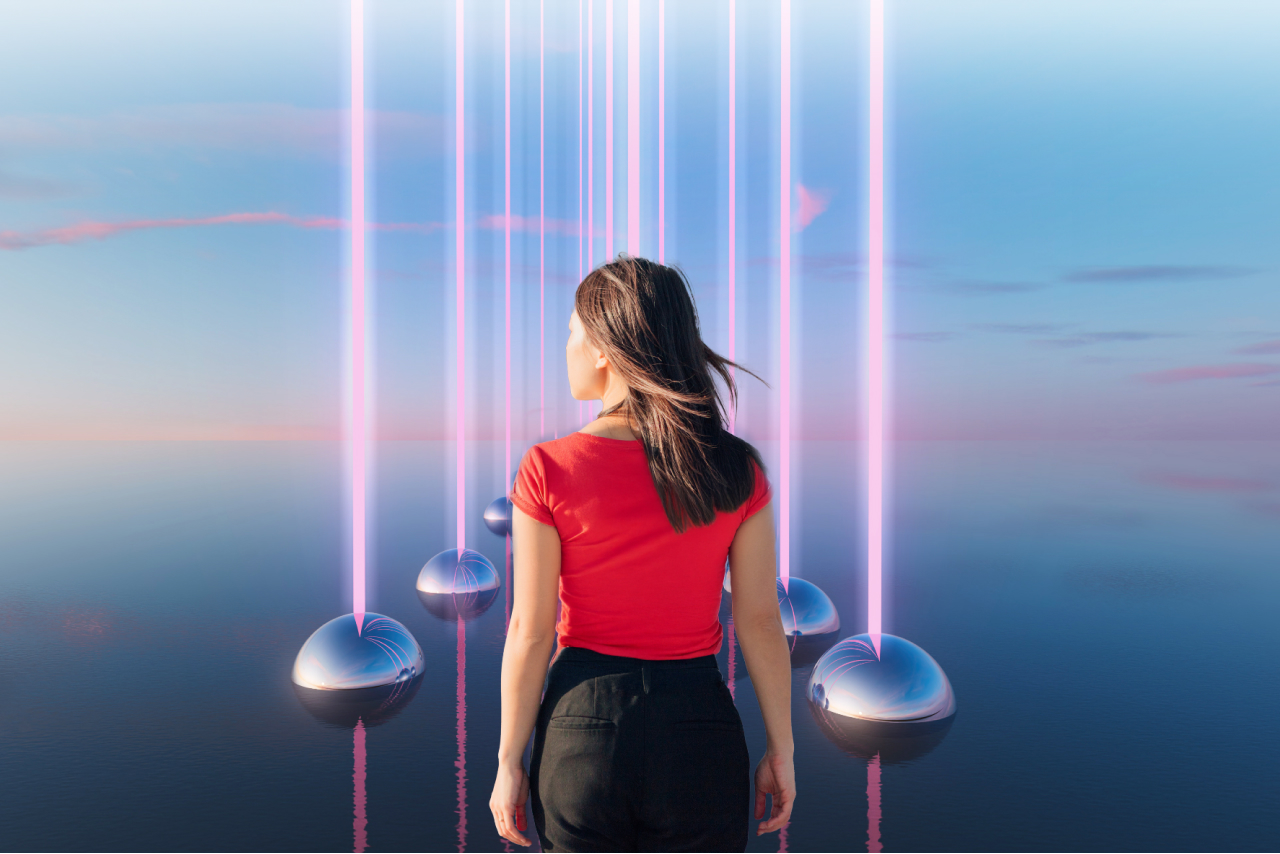 A woman stands facing away from us against a blue sky, with silver balls emanating purple light from each side