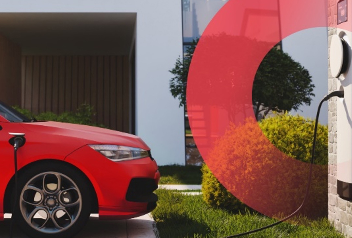 Front of red car plugged into electric charging station against a residential building
