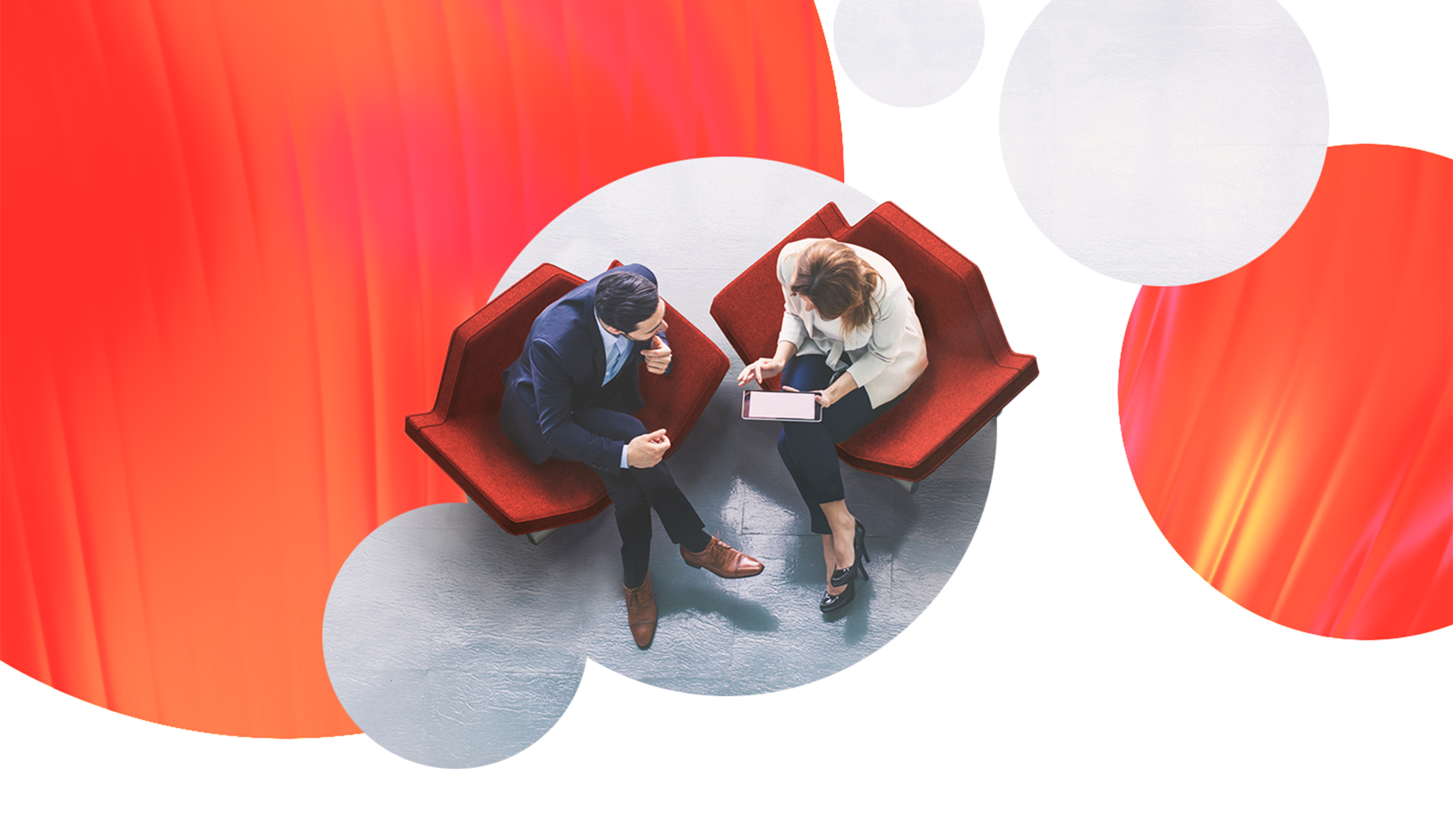 Overhead view of a man and woman collaborating together on an iPad with abstract orange circle designs around them