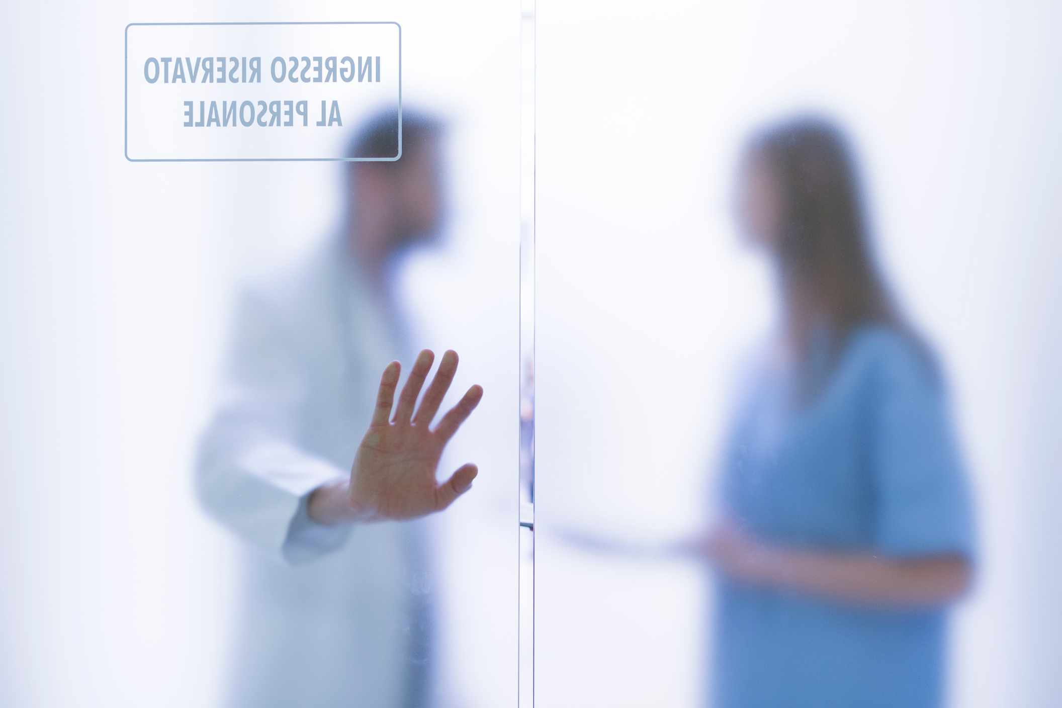 A doctor and a nurse are talking behind a closed door holding it shut with their hand.