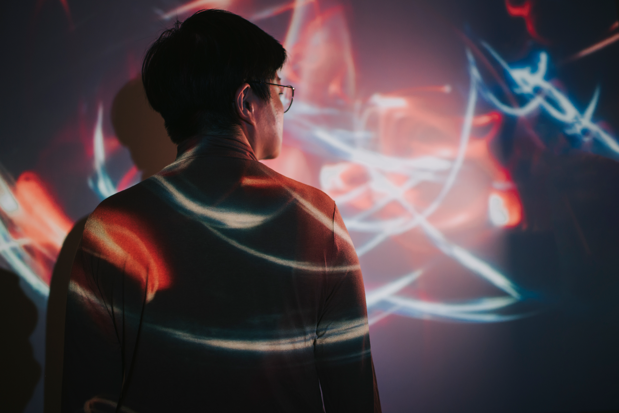 A man is positioned in front of a colorful light projection, highlighting his silhouette against the illuminated backdrop.