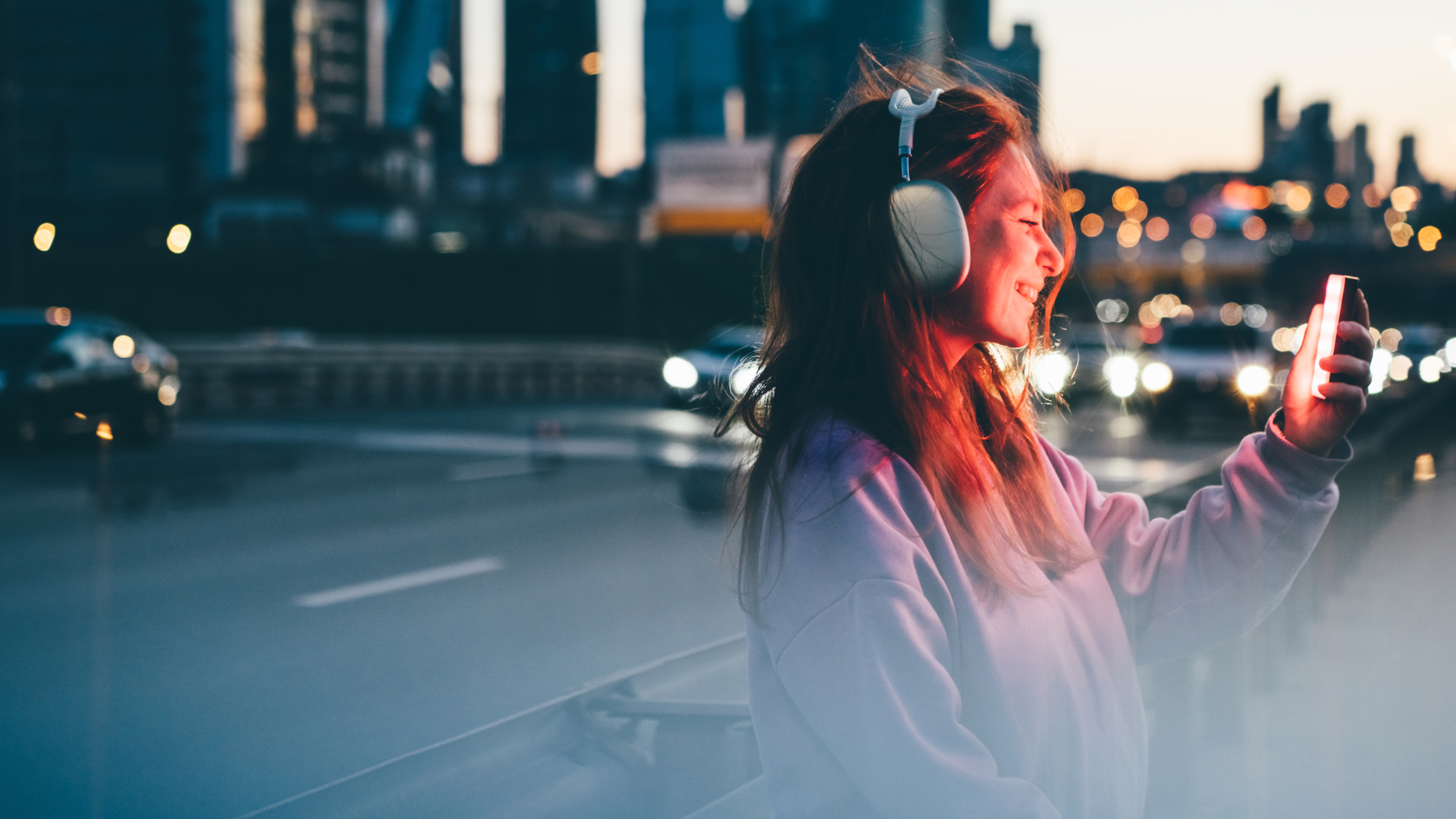 A woman wearing headphones holds a phone while walking through a bustling city street.
