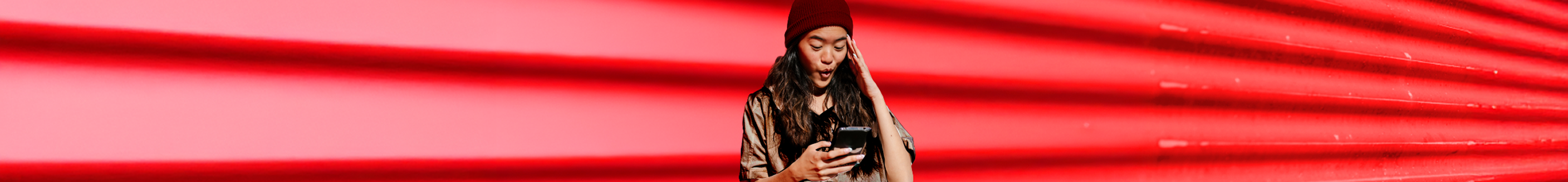 A woman stands confidently in front of a vibrant red wall, showcasing her presence against the bold background.